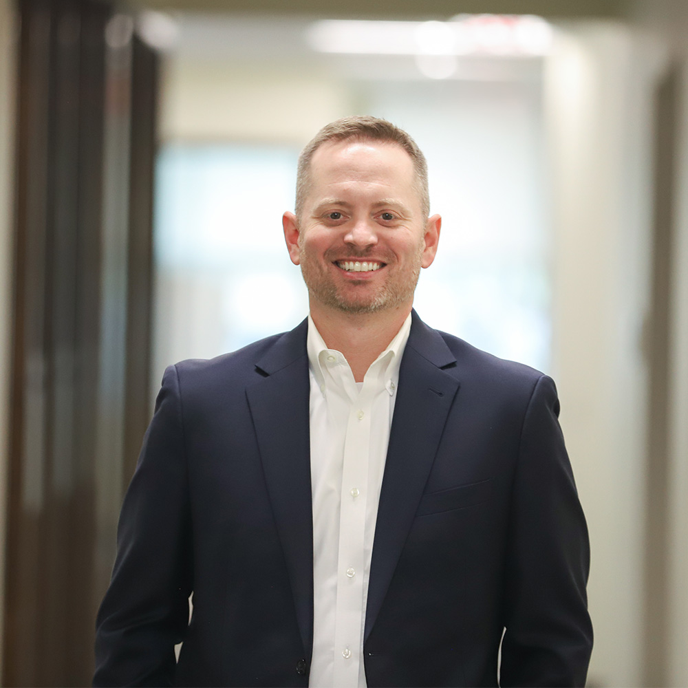 DCCU's Senior Vice President, Chief Retail Officer, Jacob Larew, stands outside and smiles for the camera in a hallway