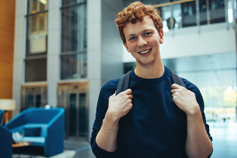 Male student wearing backpack and smiling in college lobby