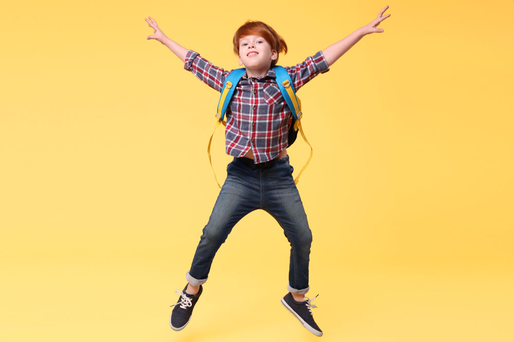 young student jumping with backpack on and yellow background